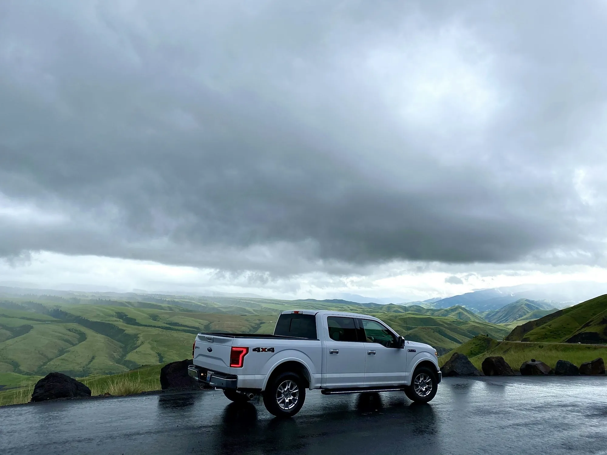 White pickup truck on a hillside road beneath a wide cloudy mountain sky